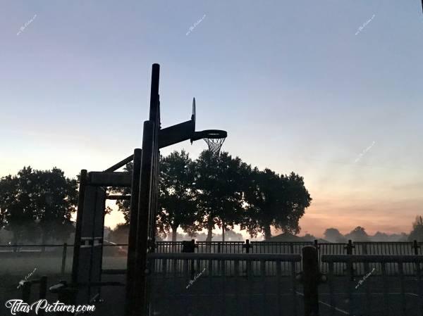 Photo Terrain de Basket : Lever du jour avec de la brume sur le terrain de Basket de la Merlatière. On aperçoit le terrain de foot derrière. 
Les couleurs étaient plus belles et plus vives en live. J’ai pas réussi à reproduire ce que je voyais, mais c’est pas trop mal comme rendu je trouve. 
Qu’en pensez-vous ?c, Terrain de Basket, La Merlatière, Brume, Lever du jour, Aurore